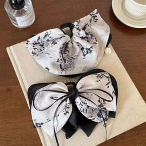 Retro ink-style floral bow hair clip set with pearl pendant on cream-colored books