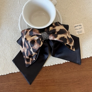 Leopard print bow hair claw clip with rhinestones shown on a rustic wooden table