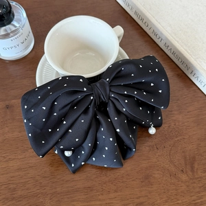 Detail of black satin bow hair clip with white heart dots and pearl pendants on wood