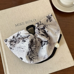 Detailed view of grey ink painting bow hair claw with pearl pendant on a book