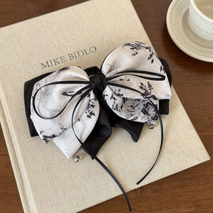 Detail of satin bow hair claw with ink floral pattern on vintage book background
