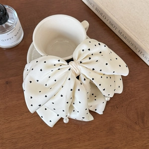 Close-up of cream satin bow hair clip with black heart dots and small pearl accents