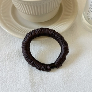 Detail of a dark brown pleated seamless hair tie with a sleek black resin buckle