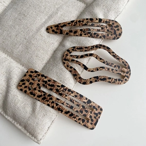 Detailed macro view of three leopard print metal hair clips on a soft beige texture