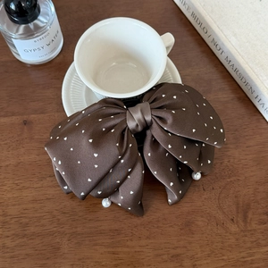 Detail of a brown satin bow hair clip with white heart dots and elegant pearl pendants