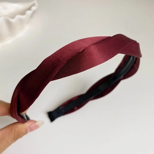 Gros plan du serre-tête en satin bordeaux avec détail torsadé et texture soyeuse