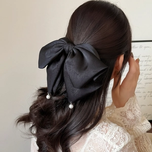 Barrette nœud géant en satin noir avec perles élégantes portée sur cheveux de modèle