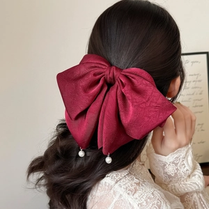 Détail d'un nœud papillon en satin bordeaux avec perles sur des cheveux bouclés