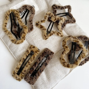 Close-up of leopard print plush hair clips in star and heart shapes on linen background