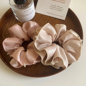 Détails de deux chouchous en satin rose avec perles délicates dans un plateau en bois