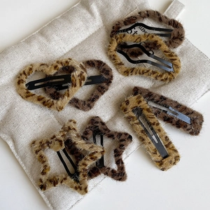Close-up of leopard print plush hair clips in heart and star shapes on a beige cushion