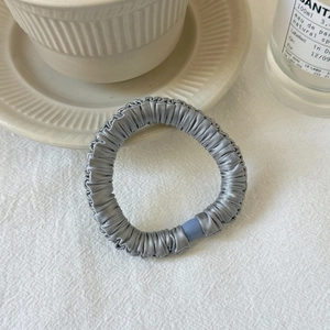 Elegant silver grey satin pleated scrunchie hair tie with silky texture on white surface