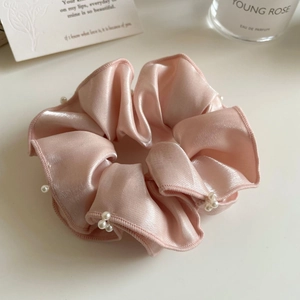 Gros plan sur un chouchou en satin rose avec perles sur un bureau blanc minimaliste