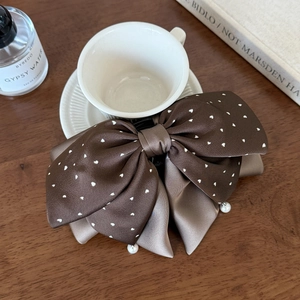 Détail d'une pince à cheveux en satin marron à pois en cœur avec un pendentif en perle