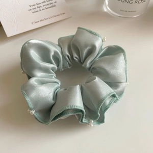Détail d'un chouchou en satin vert clair orné de petites perles d'imitation blanches élégantes