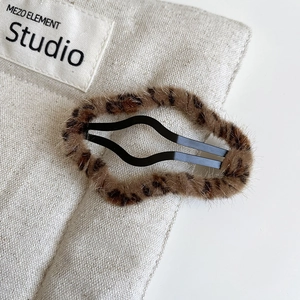 Close-up of a plush leopard print hair clip with soft faux fur on a beige linen background