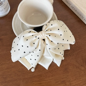 Détail d'un nœud papillon en satin crème avec imprimé cœurs et pendentifs perles