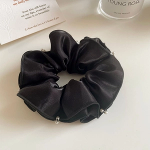 Détail du chouchou en satin noir avec perles élégantes et texture de soie douce