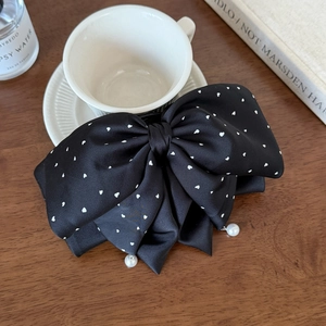 Détail d'un grand nœud à cheveux en satin noir à pois cœurs blancs et perles de nacre