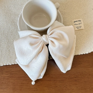 Détail d'une pince à cheveux nœud en satin beige avec perles sur table en bois