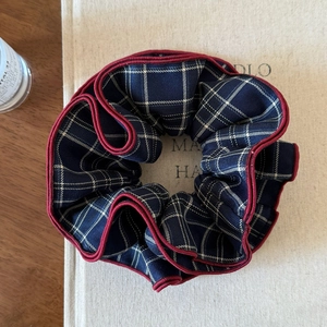 Detailed close-up of blue plaid scrunchie with red trim on a minimalist book background