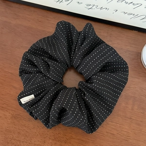Detailed view of black polka dot scrunchie with a Hand Made tag on a wooden surface