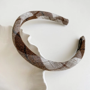 Close-up of retro plaid fabric headband with brown checkered wool texture on white tray