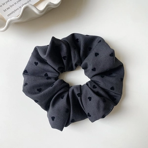 Detailstruktur eines dunkelgrauen Scrunchie mit Herzmuster auf weißem Tablett