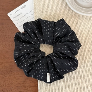 Detail of black polka dot scrunchie featuring a handmade woven label on a wooden desk