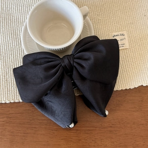 Gros plan d'un grand nœud à cheveux en satin noir avec perles sur un tapis beige texturé