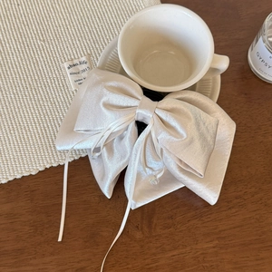 Detail of elegant cream satin bow hair clip with ribbons on a rustic aesthetic wooden desk