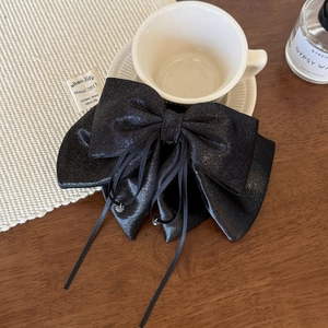 Close-up of elegant black glitter bow hair clip with ribbons on a minimalist desk set