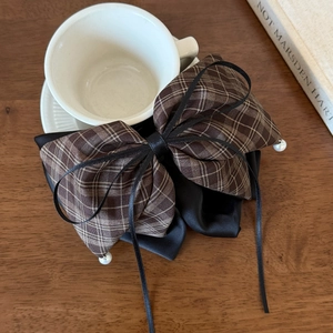 Detail view of a plaid bow hair clip with pearls hanging on a white ceramic cup