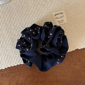Gros plan d'un chouchou bleu marine à fleurs blanches posé sur une table en bois rustique