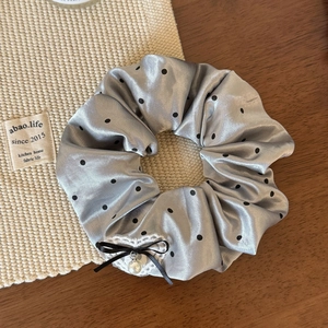 Détail d'un chouchou en satin argenté à pois avec dentelle et pendentif perle