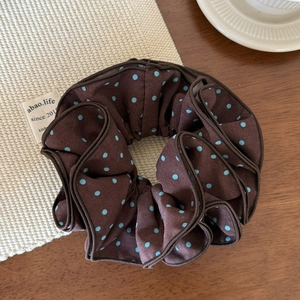 Detailed view of a dark brown polka dot scrunchie on a soft cream texture background