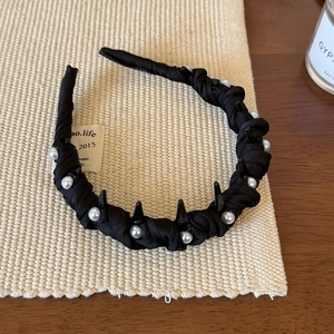 Detail of black fabric headband with white pearls and black rivets on a woven mat