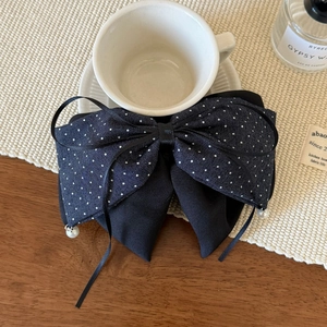 Detail of a large black polka dot bow hair clip with pearls on a wooden desk setup