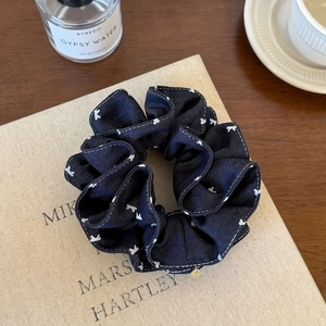 Navy blue polka dot scrunchie with white bow patterns and small gold charm detail