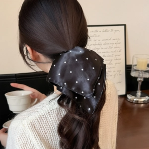 Elegant black silk scrunchie with white polka dots tied on wavy hair in French cafe setting