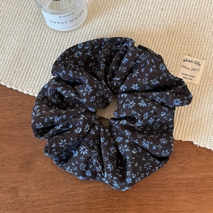 Détail d'un chouchou floral marron foncé avec fleurs bleues sur une table en bois