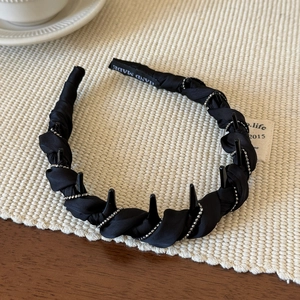 Détail d'un serre-tête en tissu plissé noir avec dents antidérapantes et perles argentées