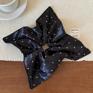 Close-up of black satin scrunchie with white polka dots and elegant long ribbon detail