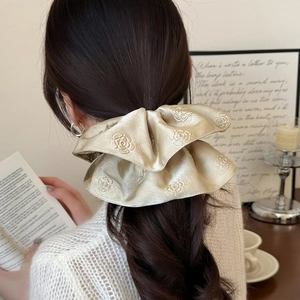 Detailed shot of a champagne silk scrunchie with rose jacquard on a model's hair