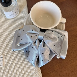Detail showing grey satin bow hair clip with black polka dots and hanging pearls