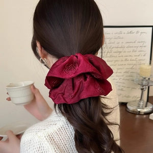 Detailed macro view of wine red satin hair scrunchie with elegant rose jacquard patterns