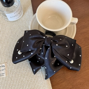 Close-up of black polka dot bow hair claw with elegant pearl charms on satin fabric