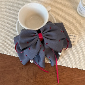 Dettaglio fiocco grigio con cuori rossi e perle pendenti su tappetino in tessuto
