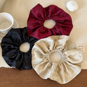 Detail of three silk jacquard scrunchies with rose patterns in red, black, and beige colors