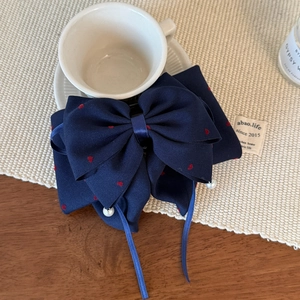 Dettaglio del fermaglio a fiocco blu scuro con cuori rossi e perline su un tavolo